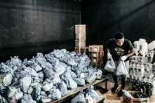 Pessoa carrega cesta basica em galpão com várias cestas basicas 