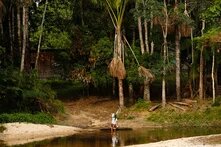 Pessoa de comunidade ribeirinha coletando água na margem de um rio cercado pela densa vegetação da Floresta Amazônica