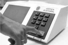 Uma pessoa aperta tecla da urna eletrônica brasileira. Foto em preto e branco.