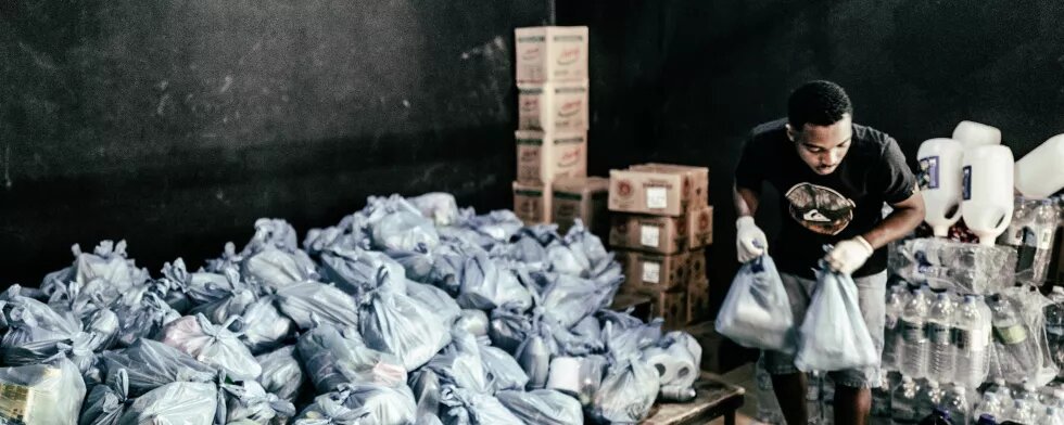 Pessoa carrega cesta basica em galpão com várias cestas basicas 