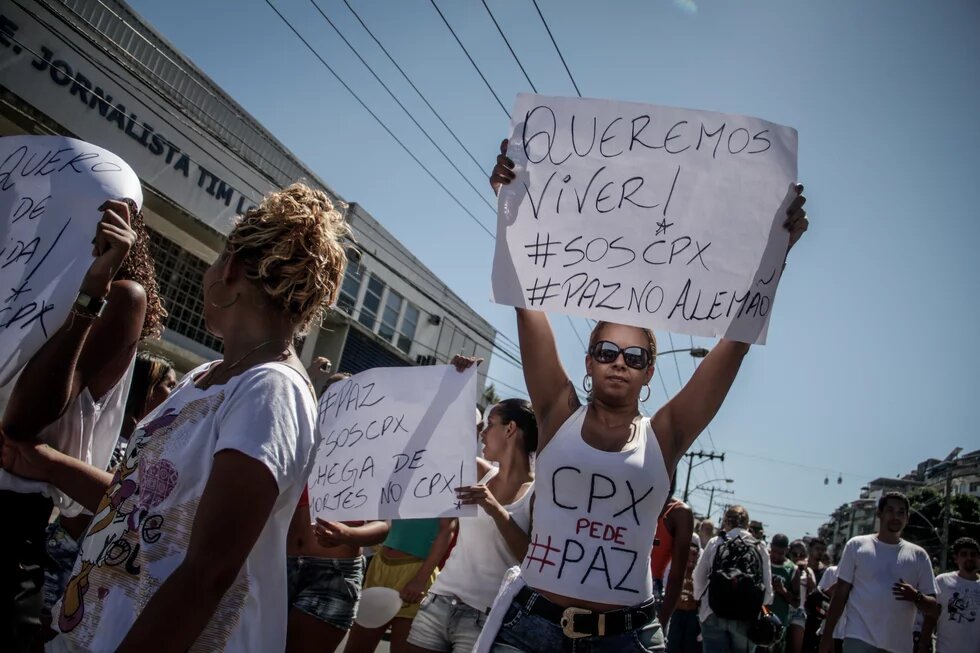 Mulher levanta cartaz com os dizeres "Queremos viver! SOS Complexo, Paz no Alemão", em protesto por paz no Complexo do Alemão em 2015.