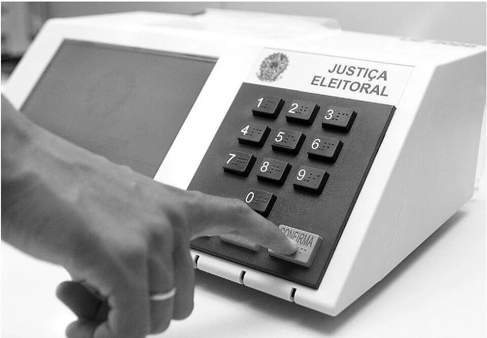Uma pessoa aperta tecla da urna eletrônica brasileira. Foto em preto e branco.